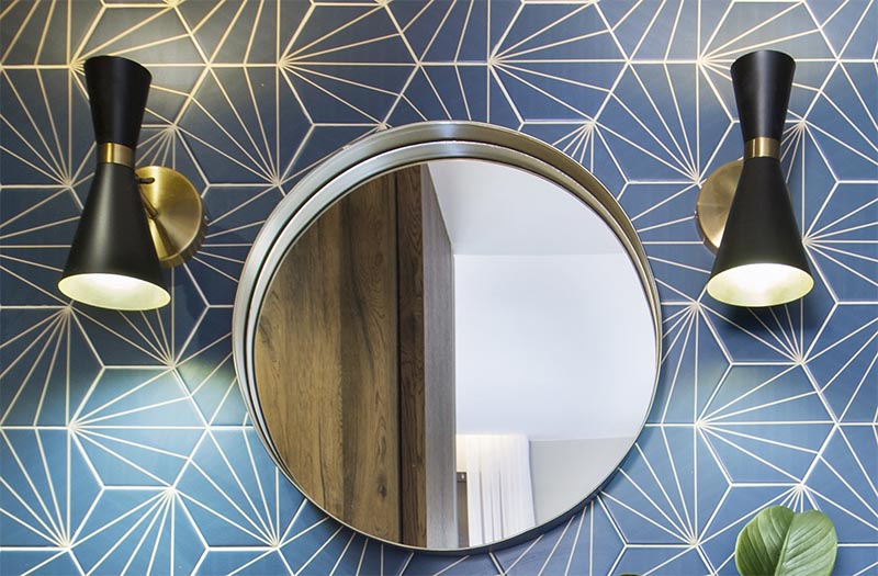 This modern blue bathroom has eye-catching starburst patterned tiles, rose gold tap and faucet, a concrete countertop, black and gold lighting, and a round mirror. #BlueBathroom #StarburstTile #ModernBathroom #BathroomIdeas