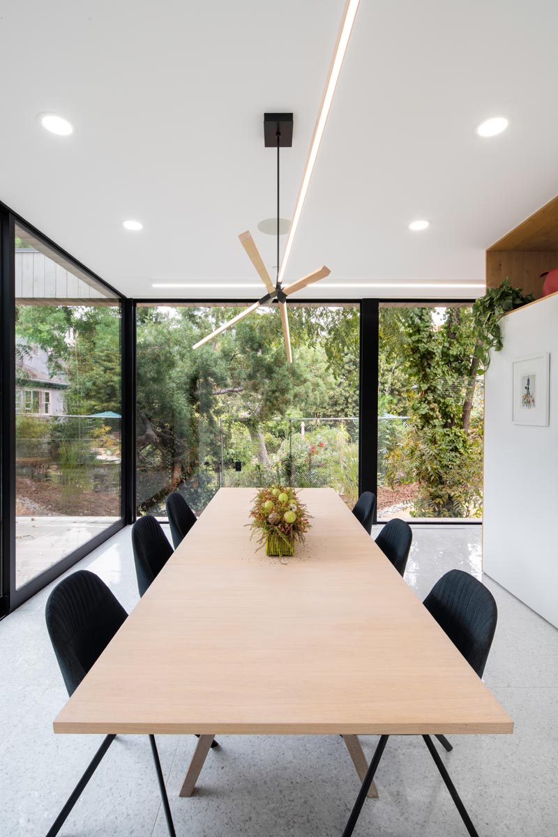 This modern dining room has floor-to-ceiling glass walls look out to the trees, while inside, the wood dining table complements the wood lighting above it. #ModernDiningRoom #GlassWalls