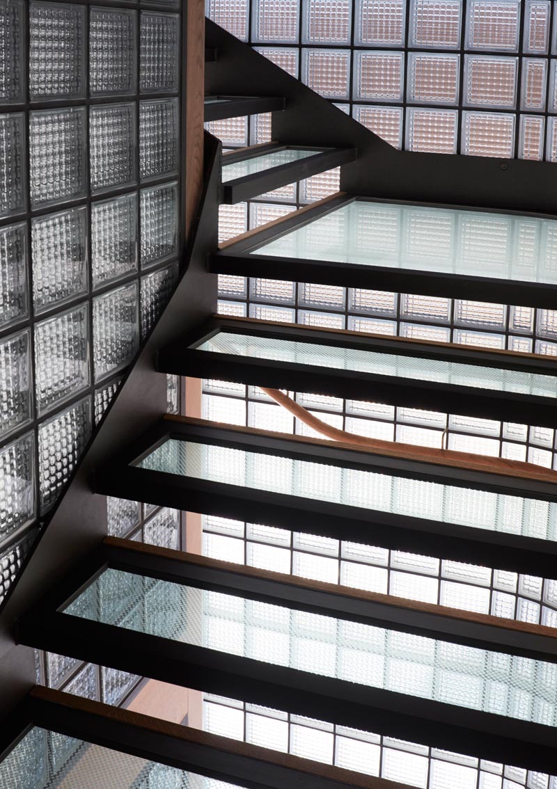 This modern house features a stairwell surrounded by glass blocks with black grout, and steel, wood, and glass treads. #ModernGlassBlock #GlassBlock #Stairs #Stairwell