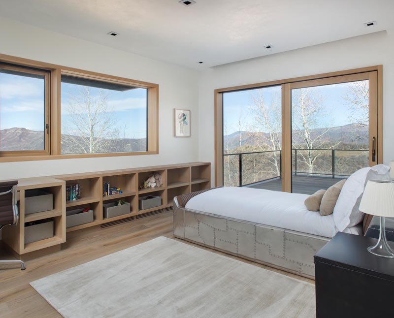 In this modern children's bedroom, a row of shelving lines the wall and merges with a desk, while a sliding glass door opens to a balcony.  #ChildrensBedroom #KidsBedroom #Shelving