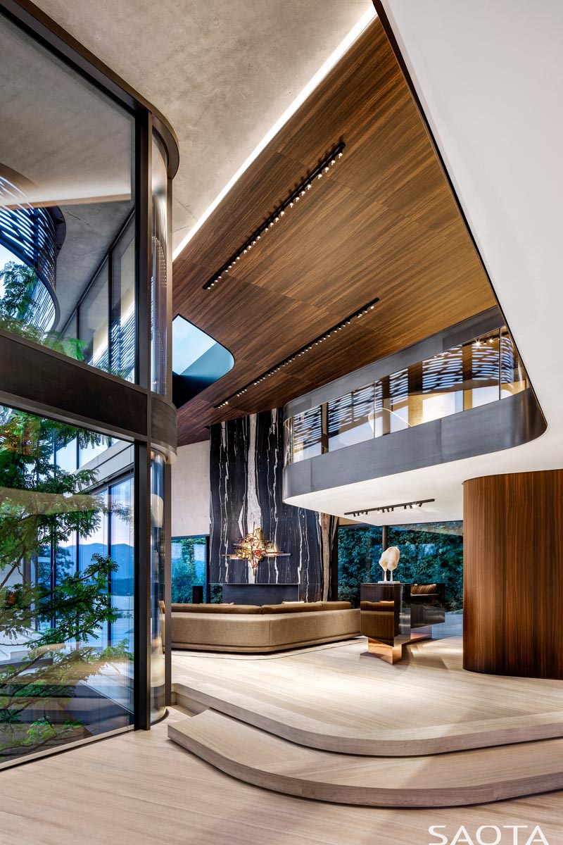 This modern double height living room has a wood ceiling with accent lighting, while a black and white stone wall adds to the feeling of height with its vertical lines. #LivingRoom #StoneWall #WoodCeiling #ModernInterior