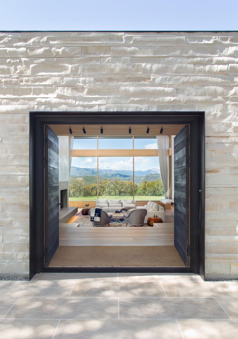 This large front door creates a dramatic entrance and contrasts the exterior staggered, remnant stone walls that are aligned with interior walls that run in a single direction, allowing light and landscape to slip past. #ModernFrontDoors #StoneWallExterior #StoneFacade