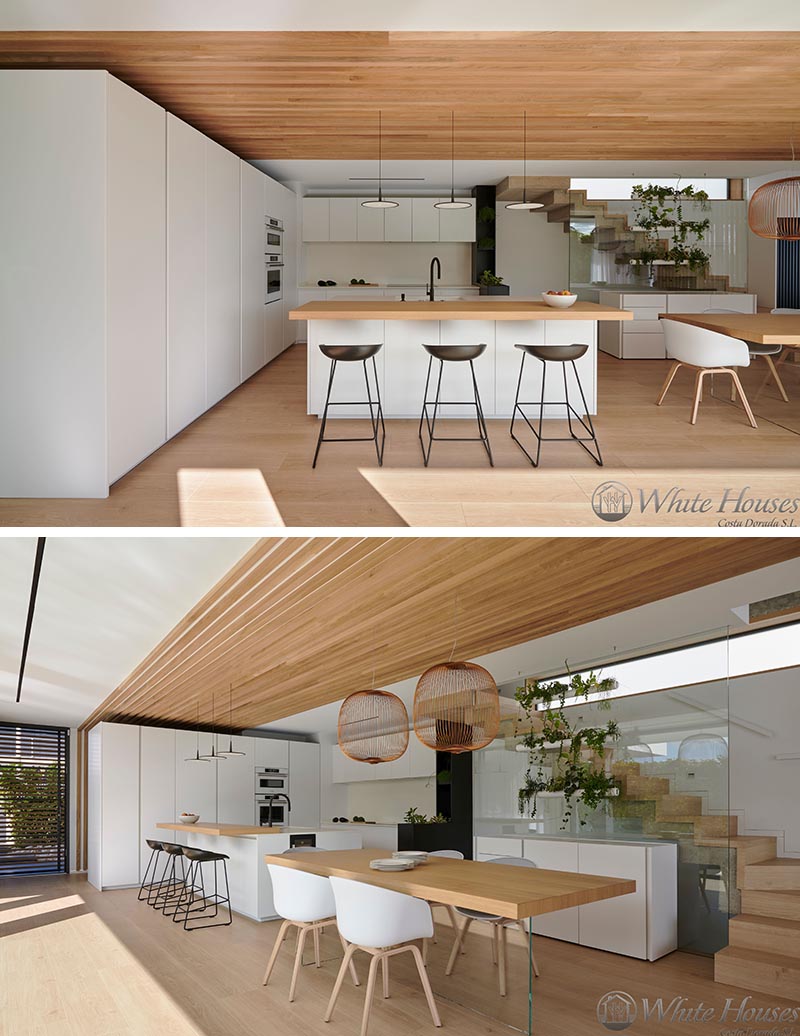 Connecting and defining this modern kitchen and dining area is a wood slat accent that travels from one wall at the end of the kitchen onto the ceiling and through to the dining area, where it becomes a partition wall, separating it from the living room. #KitchenDesign #DiningArea #WoodSlatWall #Partition #ModernKitchen