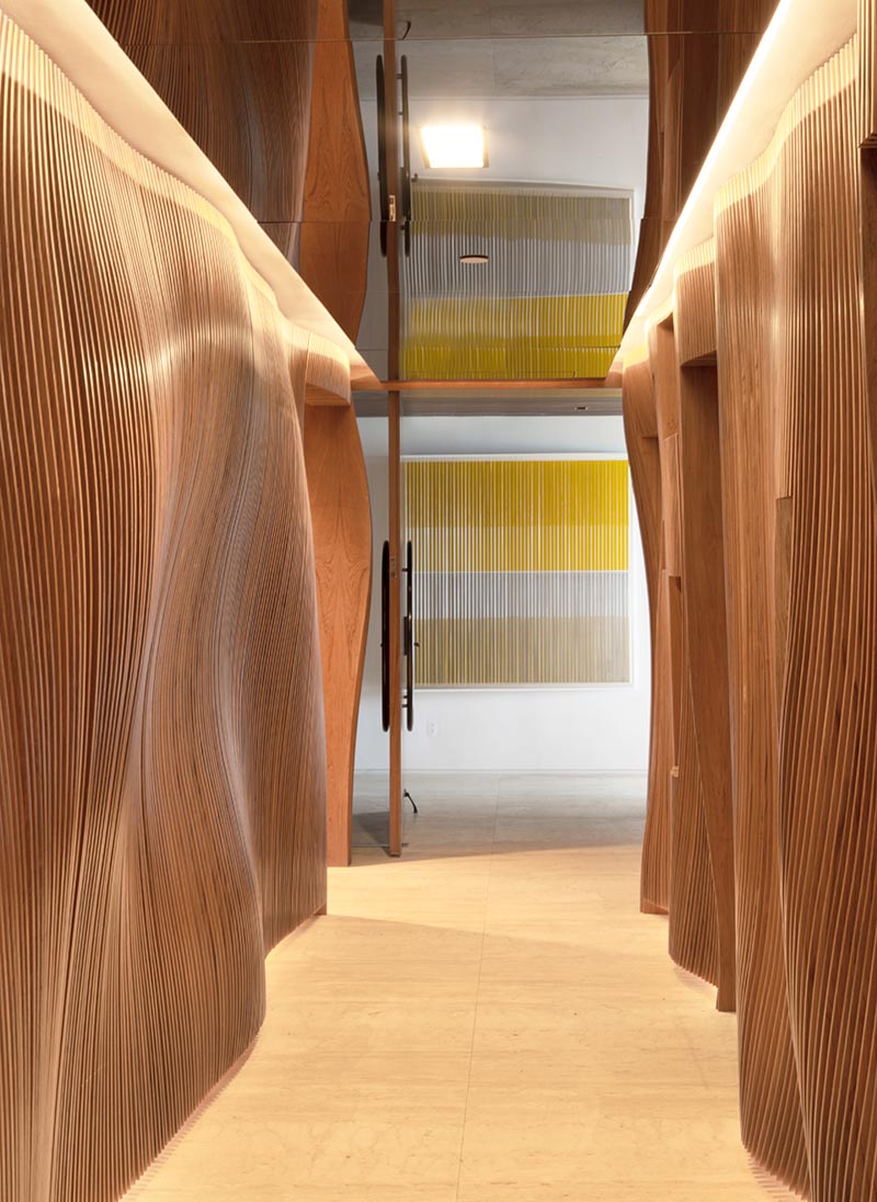 Fernanda Marques Arquitetos Associados has designed an apartment in Miami, Florida, and as part of the design, they included an eye-catching sculptural wood hallway with a mirrored ceiling. #WoodHallway #SculpturalHallway #WavyWoodWall #InteriorDesign #MirroredCeiling