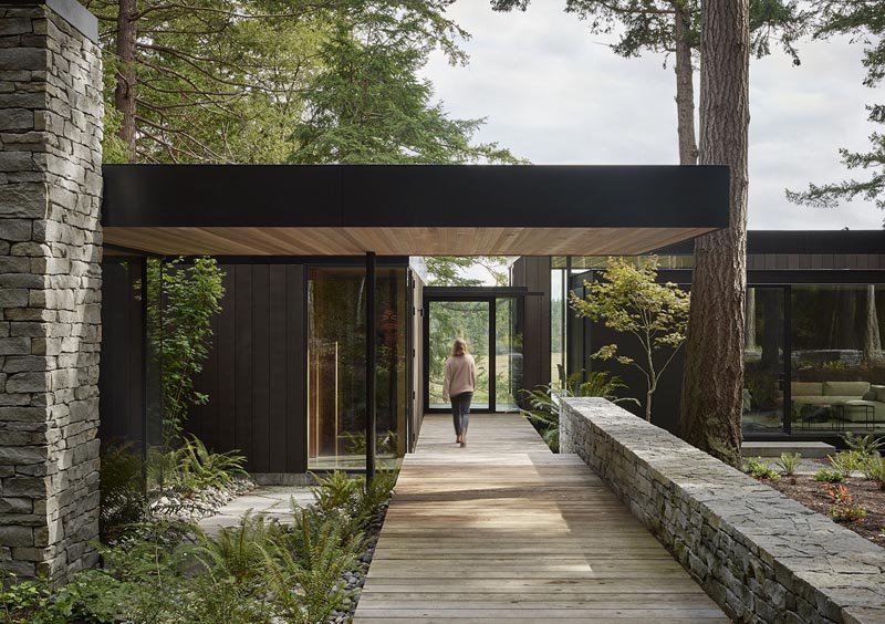 This modern house is situated on the edge of a forested hillside, overlooking chicken sheds, a weathered red barn, cattle fields, and a fishing pond. #ModernHouse #DarkWoodSiding #Architecture