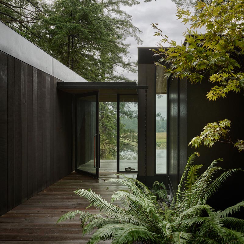 This modern house is situated on the edge of a forested hillside, overlooking chicken sheds, a weathered red barn, cattle fields, and a fishing pond. #ModernHouse #DarkWoodSiding #Architecture #Entryway