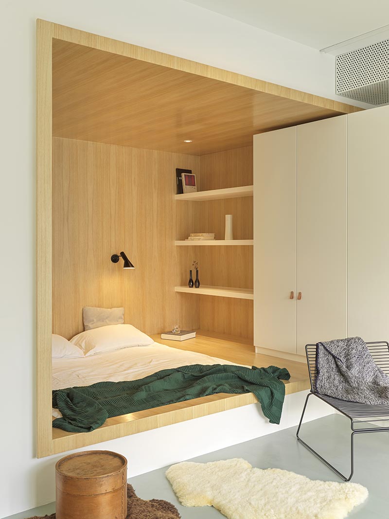 Instead of having a freestanding bed, the designers made use of an odd  shaped corner small positioned the bed within the base of its own wood-lined niche, allowing for more floor space by the large windows. #BedroomIdea #BedNook #BedNiche #BuiltInBed #InteriorDesign #ModernBedroom