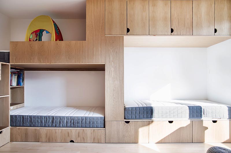 This modern kids bedroom has high ceilings, a sliding wood door, an open space for play, a wall of cabinets, and a bunk bed designed for three. #BunkBed #KidsRoom #ChildrensBedroom #Cabinets #BedDesign