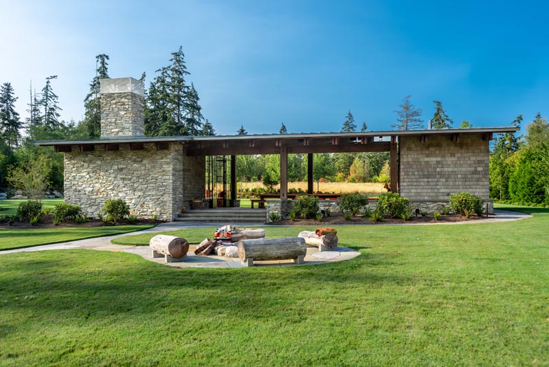 Stairs and a path lead from a large garden pavilion to a firepit with log seating.