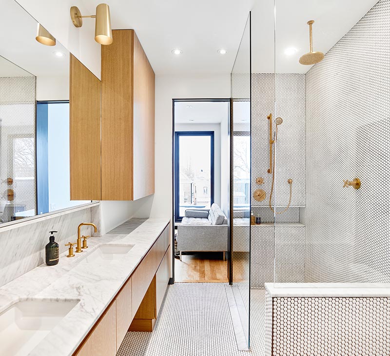 A modern master bathroom with hardware free wood cabinets, a marble vanity with dual sinks, brass fixtures, penny tiles, and custom-build niches. #ModernBathroom #MarbleVanity #BrassFixtures #PennyTiles #ShowerNiche