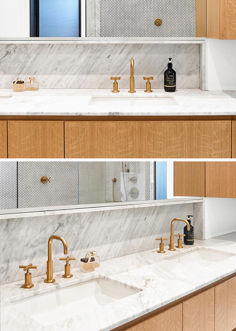 For the vanity in this modern bathroom, hardware free wood cabinets have been paired with light grey marble countertops, white under-mount dual sinks, and brass fixtures. #ModernBathroomVanity #MarbleVanity #BrassFixtures #WoodCabinets