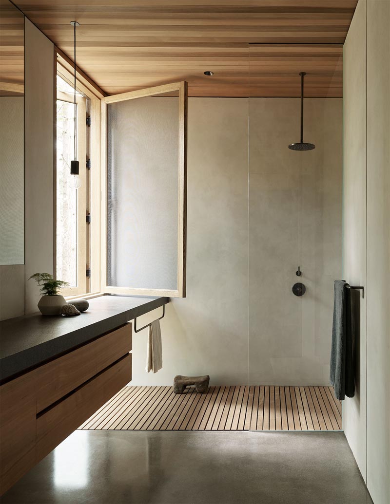 In this modern bathroom, there's a large window providing natural light for the shower, while a floating vanity with wood cabinetry complements the wood ceiling. #BathroomDesign #ModernBathroom