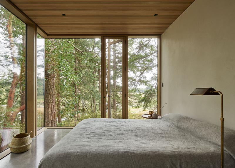 In this minimalist bedroom, the floor-to-ceiling windows provide an uninterrupted view of the surrounding trees. #ModernBedroom #Windows #WoodCeiling