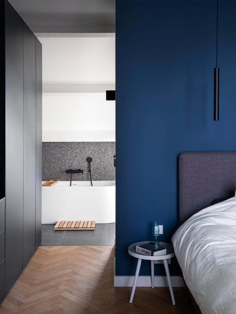 In this modern master bedroom, a royal blue accent wall has been combined with black cabinetry, white trim, and herringbone wood floors. #MasterBedroom #BlueWalls #BedroomDesign