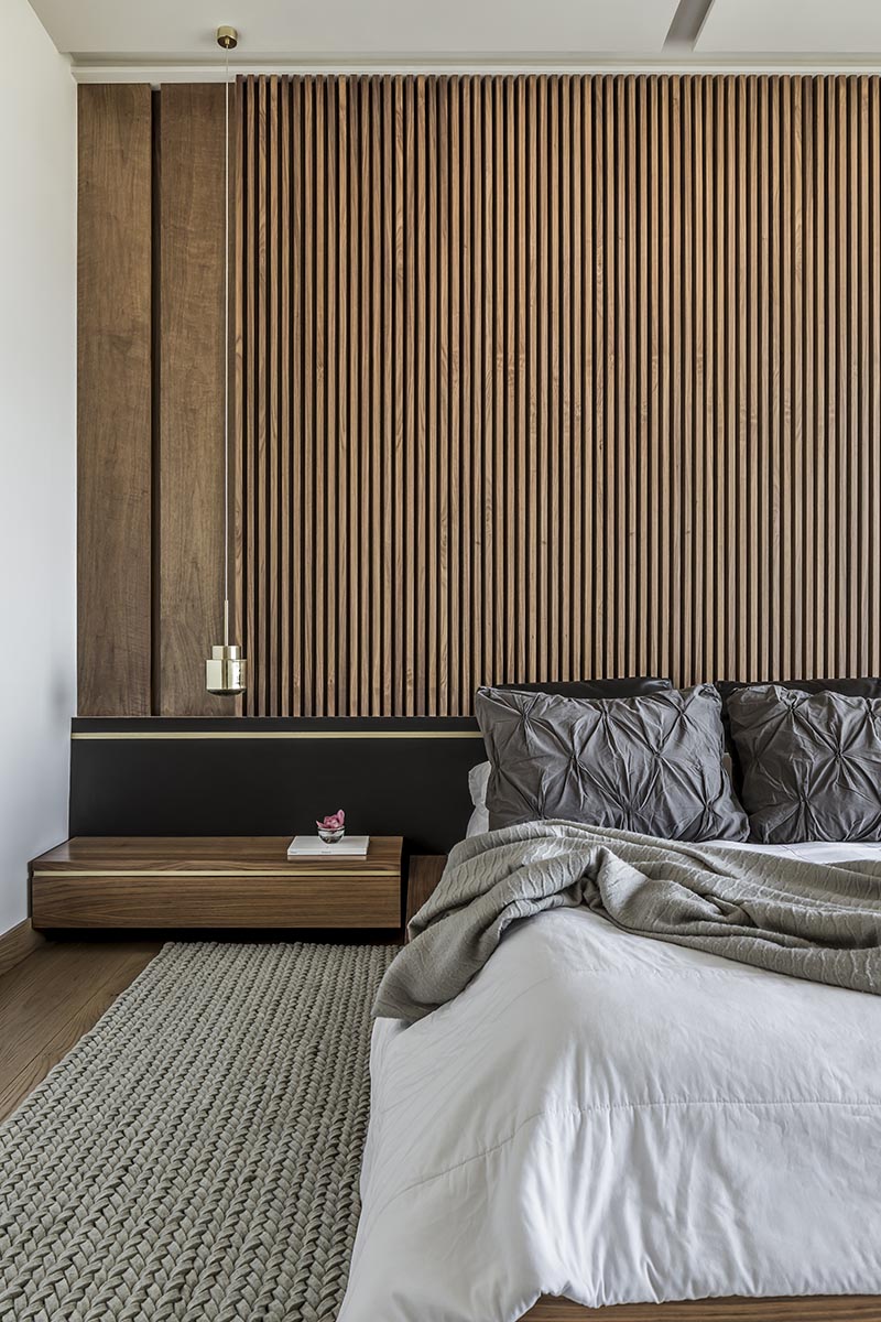 One of the key design choices of this modern bedroom was a large wood slat accent wall that immediately adds a sense of warmth to the room and provides a backdrop for the bed. It's complemented by low profile wood bedside tables, a black headboard, and hanging metallic pendant lights that acts as bedside lamps. #ModernBedroom #BedroomIdeas #WoodAccentWall #WoodSlatWall