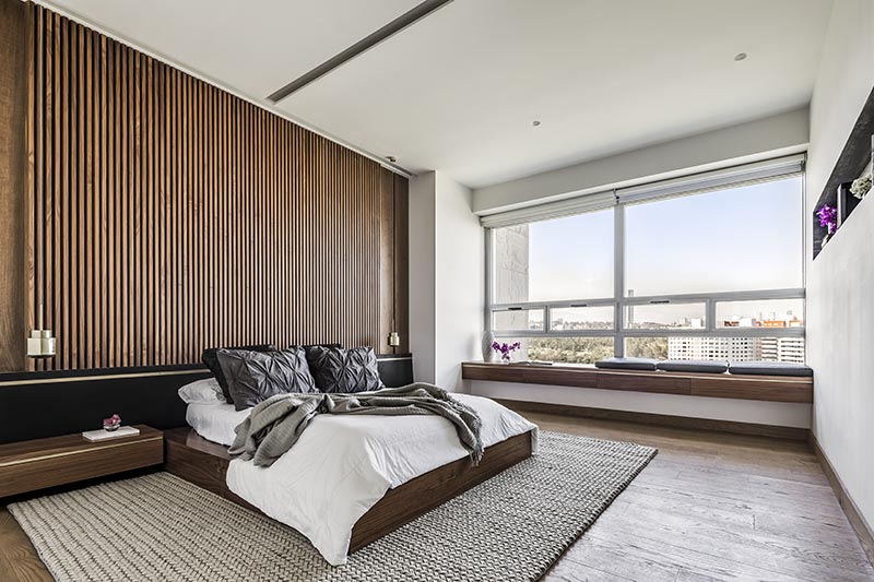 One of the key design choices of this modern bedroom was a large wood slat accent wall that immediately adds a sense of warmth to the room and provides a backdrop for the bed. It's complemented by low profile wood bedside tables, a black headboard, and hanging metallic pendant lights that acts as bedside lamps. #ModernBedroom #BedroomIdeas #WoodAccentWall #WoodSlatWall