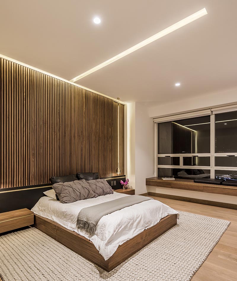 In a modern bedroom, hidden lighting in the ceiling and around the edges of this wood accent wall helps to provides a soft ambient light to the room. #Lighting #BedroomLighting #BedroomIdeas #ModernBedroom