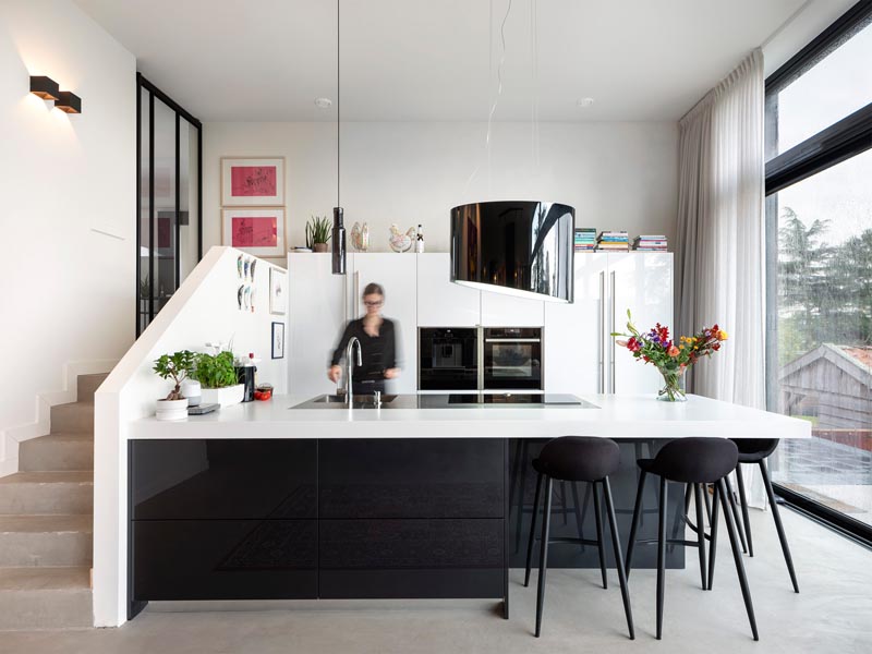 Inside this modern house, steps lead from the front entryway down into the kitchen, that has black accents contrasting the white cabinets and countertop. #ModernKitchen #BlackAndWhite #BlackAndWhiteKitchen #KitchenDesign