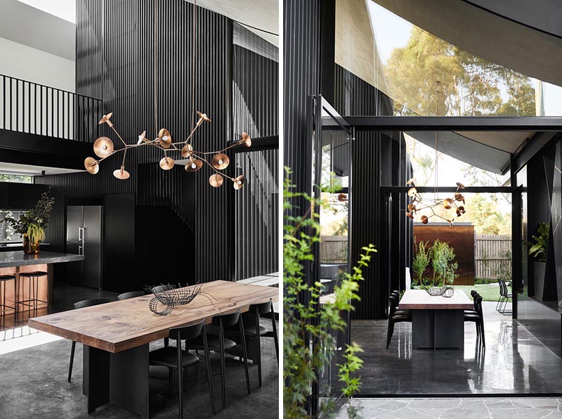 Adjacent to the kitchen in this modern house is the dining area, with a large sculptural light positioned directly above the wood and black metal table. #DiningTable #DiningArea