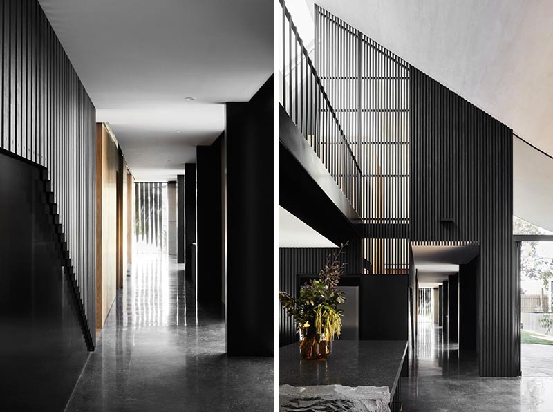 Inside this modern house, there's a long hallway lined with blackened timber slats that leads from the front door, through to the open plan kitchen and dining room. #ModernInterior #Hallway #BlackInterior