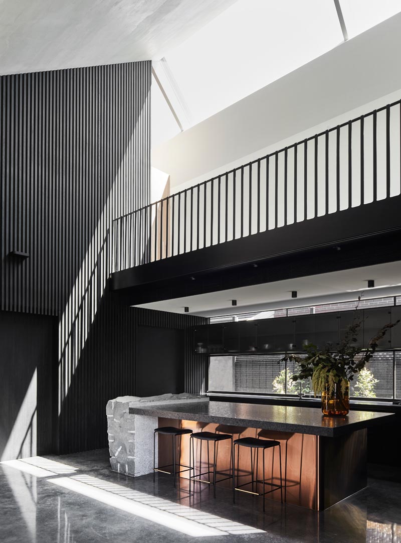 In this modern kitchen, black cabinets are paired with dark countertops, grey stone, and a rose-tone metal accent. #ModernKitchen #BlackKitchen #KitchenIsland