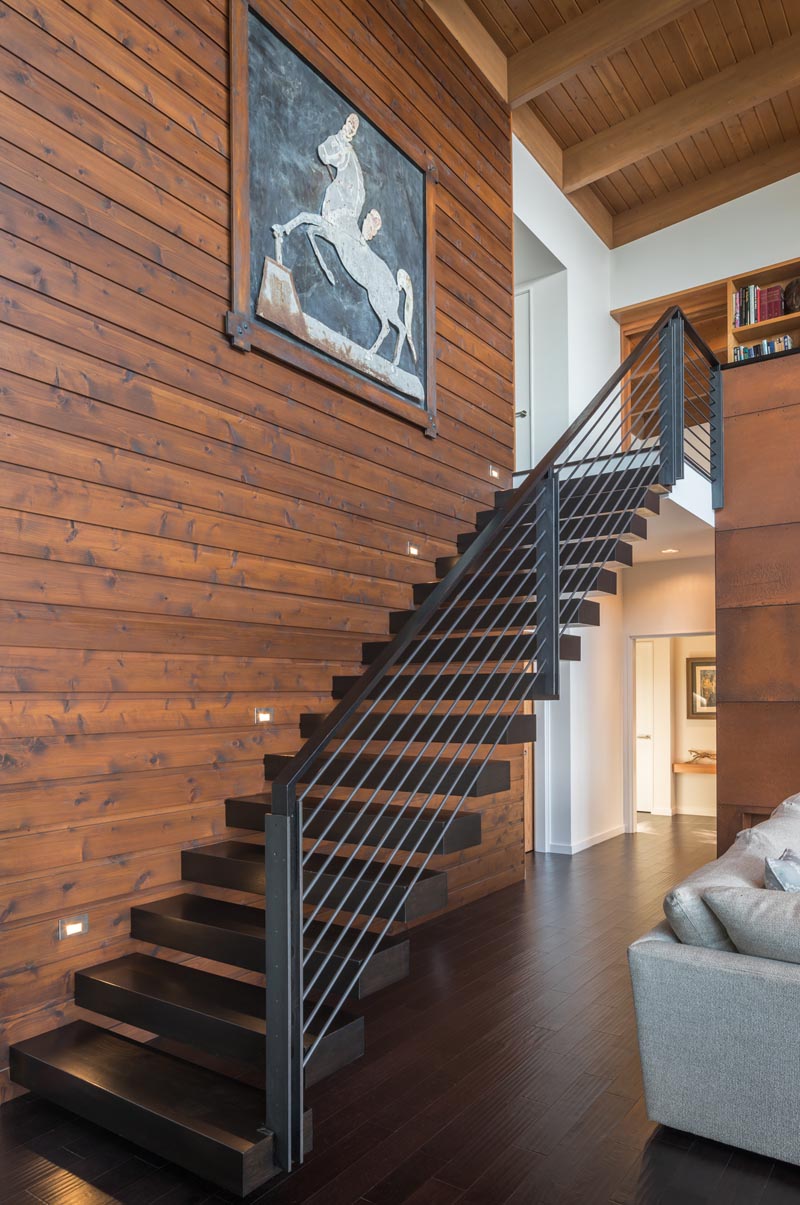 Cantilevered wood “floating” stair treads lead to a library overlooking the double-height living and dining space below. #Stairs #CantileveredStairs #ModernStairs