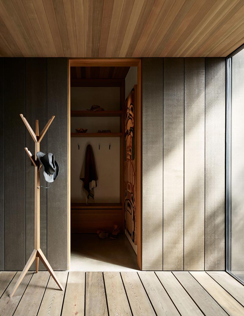 Stepping inside this modern house, and, different shapes of wood have been used to create a warm and welcoming atmosphere. Just off the front door is a mud room with a place to hang jackets and store shoes. #ModernEntryway #WoodWalls #WoodCeiling #Mudroom