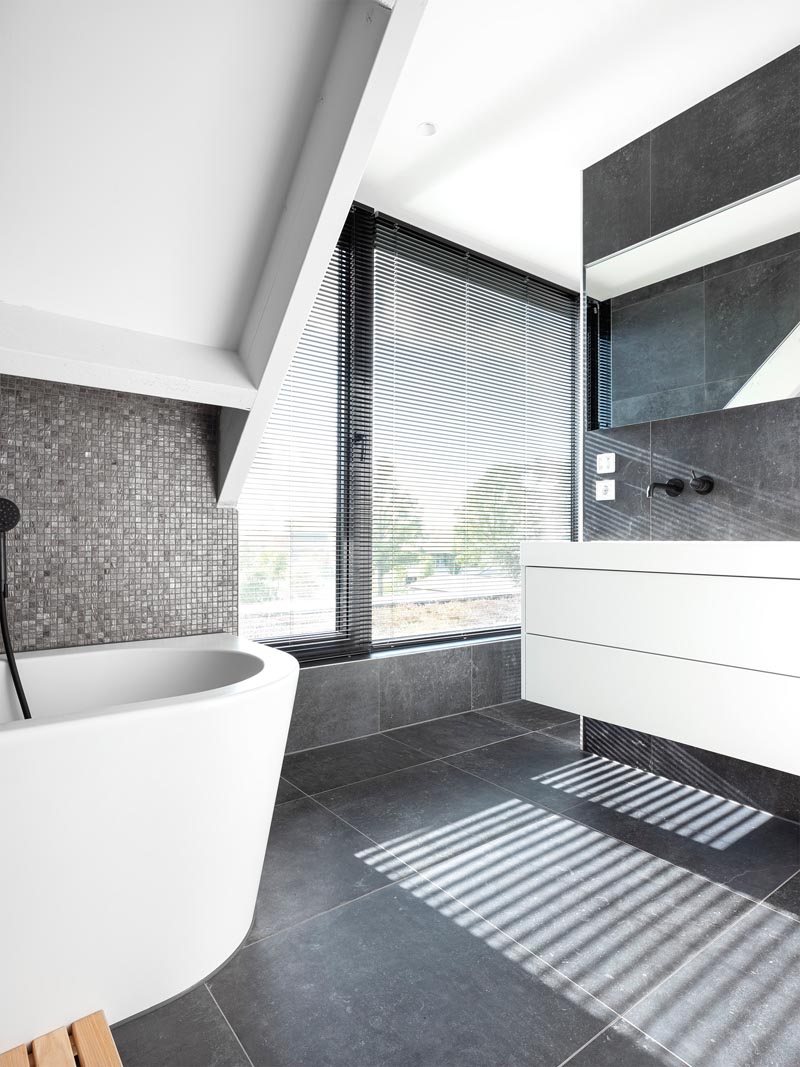 In this modern master bathroom, large format grey tiles cover the floor and walls, while small metallic grey tiles provide a backdrop for the bath. A door opens to a small outdoor space overlooking the back garden. #MasterBathroom #GreyAndWhiteBathroom #BathroomDesign