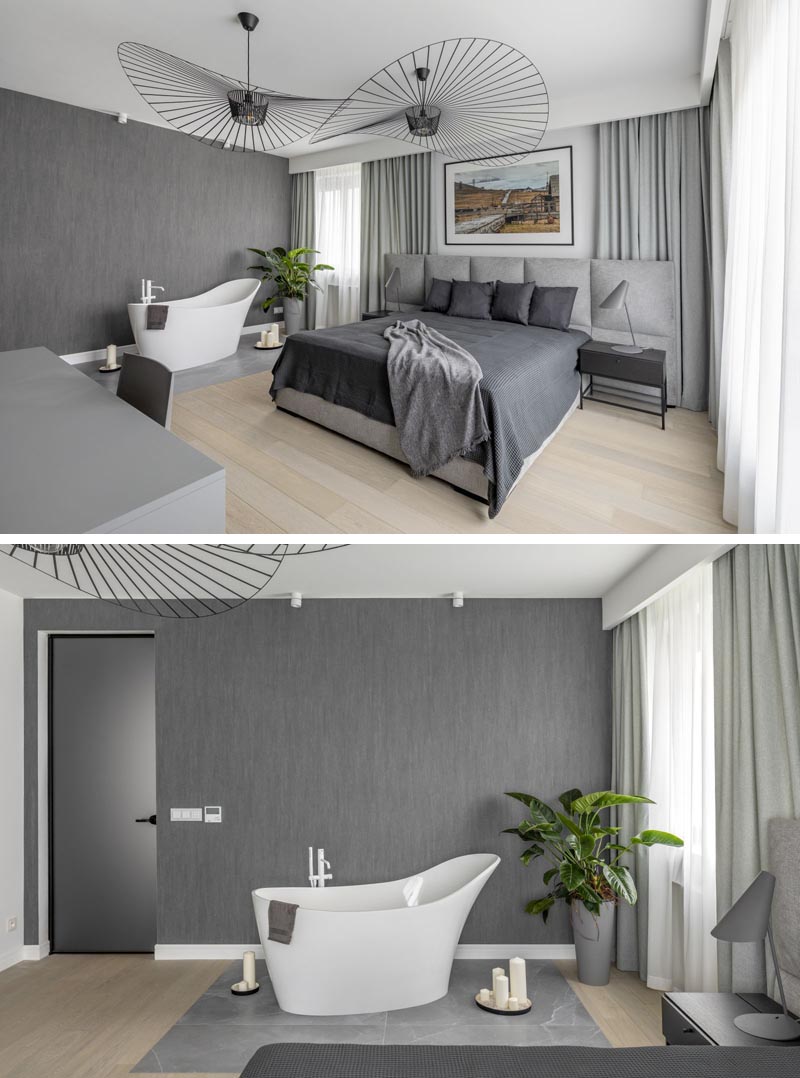 In this modern bedroom, sculptural lighting fixtures add an artistic flair, while a grey-tiled section of the floor is home to a freestanding bathtub. #ModernBedroom #BedroomWithBathtub #GreyBedroom
