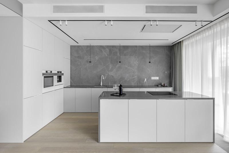 This modern kitchen showcases minimalist white cabinets, grey countertops, and a grey backsplash that covers the wall. #ModernWhiteKitchen #ModernKitchen #GreyCountertops