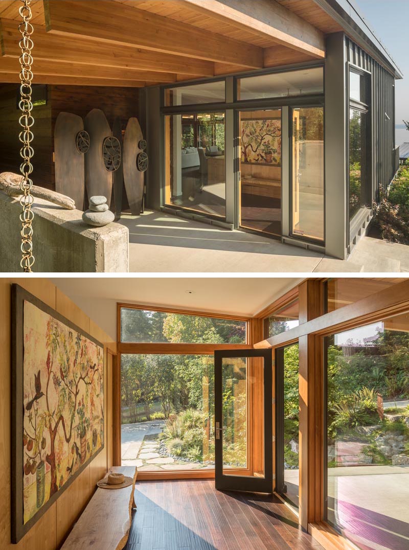 The front covered entryway at the side of this modern Pacific-Northwest house has a rainchain, sculptural accent, and a small foyer with artwork and wood floors. #Entryway #Foyer #Architecture
