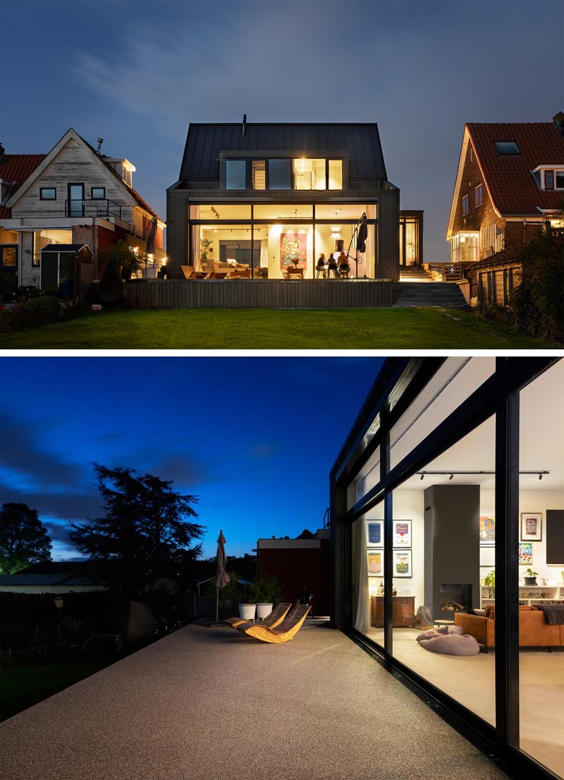 The rear of this modern black house has a large glass wall that opens up to a deck and the sloped yard. #ModernHouse #Windows #Architecture