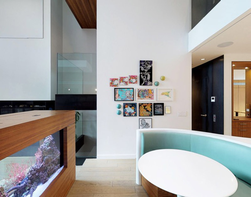 The custom-designed white Corian island countertop in this modern kitchen, has a rectangular shape at one end, before transitioning into a curved split design that wraps around the soft blue banquette seating that makes up the integrated breakfast nook. #KitchenDesign #ModernKitchen #BreakfastNook #BanquetteSeating #KitchenIsland