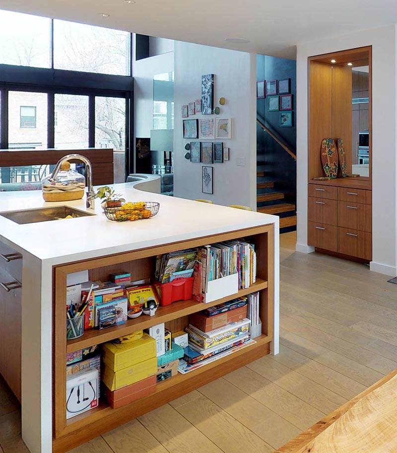 This modern kitchen island features a built-in bookshelf, an undermount sink, and a curved breakfast nook. #KitchenIsland #KitchenDesign #ModernKitchen #KitchenShelving