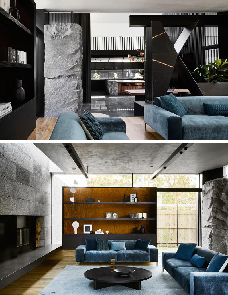 In this modern house, a stone element separates the dining area and the living room where colorful soft furnishings creating a strong variation in texture and finish. The hearth of the fireplace travels from one side of the living room to the other, and connects to the outdoor space. #ModernInterior #LivingRoom #BlueCouches #STone #DarkInterior