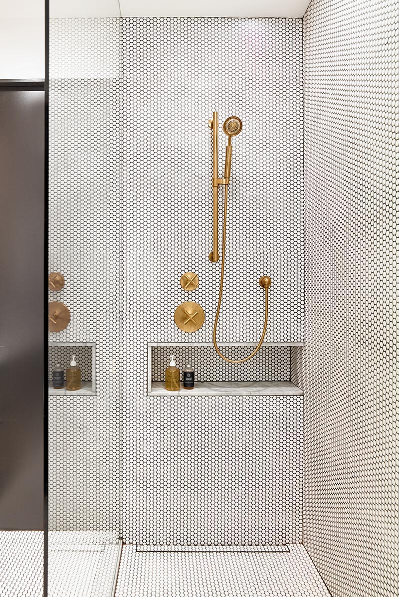 A modern shower with a glass screen, white penny tiles with contrasting black grout, a marble lined shower niche, and brass fixtures. #ModernShower #PennyTile #BrassFixtures #ShowerNiche