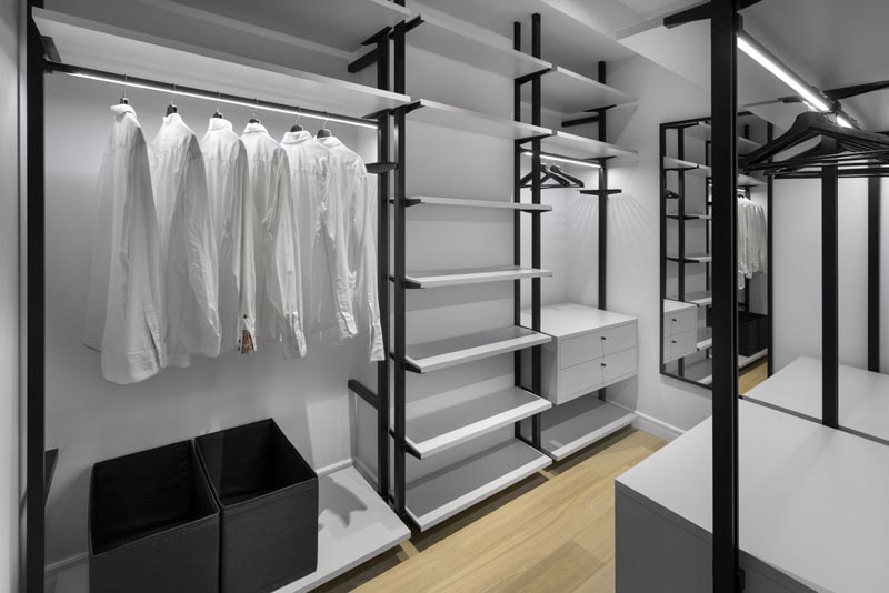This modern and large walk-in closet has plenty of room for hanging clothes and storing shoes. A mirror on the end wall makes the space feel larger, while the rods have hidden lighting to show off the clothes and brighten the space. #WalkInCloset #Closet #Wardrobe #WalkInWardrobe