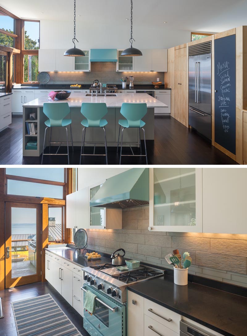 In this modern kitchen, a large white island provides space for three counter stools that complement the color of the light blue oven, while a chalkboard, dark counters, and back lighting provide a contrasting element. #WhiteKitchen #ModernKitchen