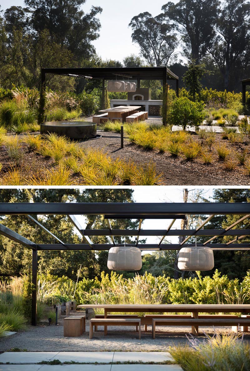 An outdoor dining area underneath a pergola with hanging lights and a wood fire pizza oven.