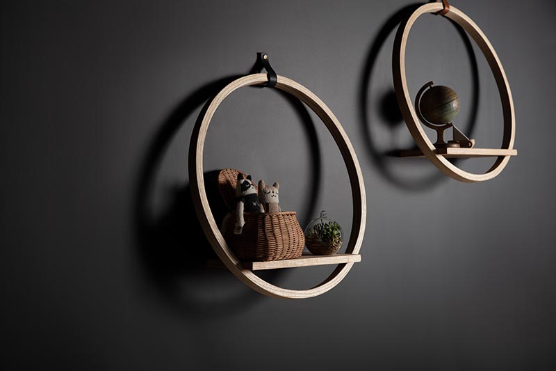 A modern round wood shelf with a leather hook and ledge for displaying decorative items.