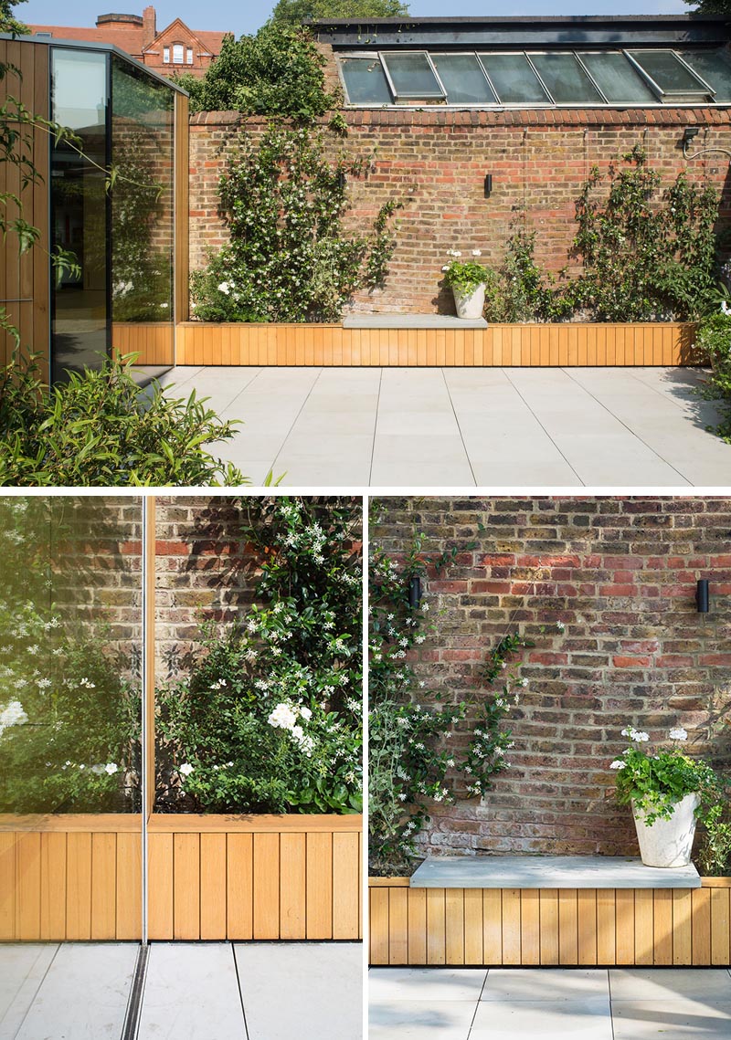 Oak clad planters extend along the garden wall and connect the building with the existing landscape. The old bricks provide a textured and warm backdrop to the new oak lining, flowers and greenery, while a small bench on top of the planter provides a place to appreciate the flowers and rest against the garden wall. #GardenIdeas #PlanterIdeas #GardenBench #ModernGarden