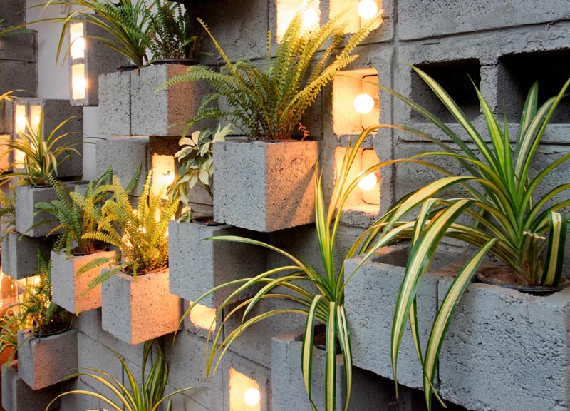 Concrete blocks were used to create this modern eye-catching accent wall, with some of them turned to become planters, slightly protruding to make room for the plants. Other blocks have been turned on their side to make room for individual light bulbs adding a soft glow of the light to the scene. #ConcreteBlockPlantWall #ConcreteBlockPlanter #CinderBlockPlanter 