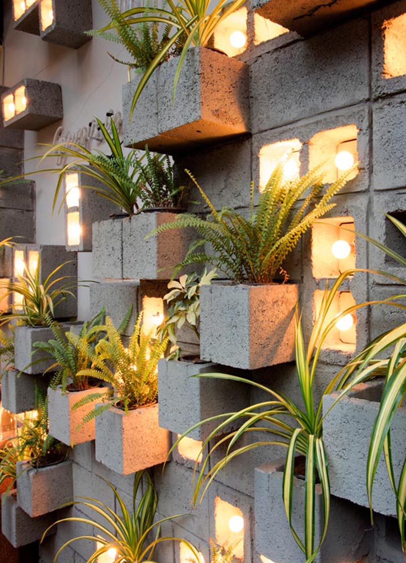 Concrete blocks were used to create this modern eye-catching accent wall, with some of them turned to become planters, slightly protruding to make room for the plants. Other blocks have been turned on their side to make room for individual light bulbs adding a soft glow of the light to the scene. #ConcreteBlockPlantWall #ConcreteBlockPlanter #CinderBlockPlanter 