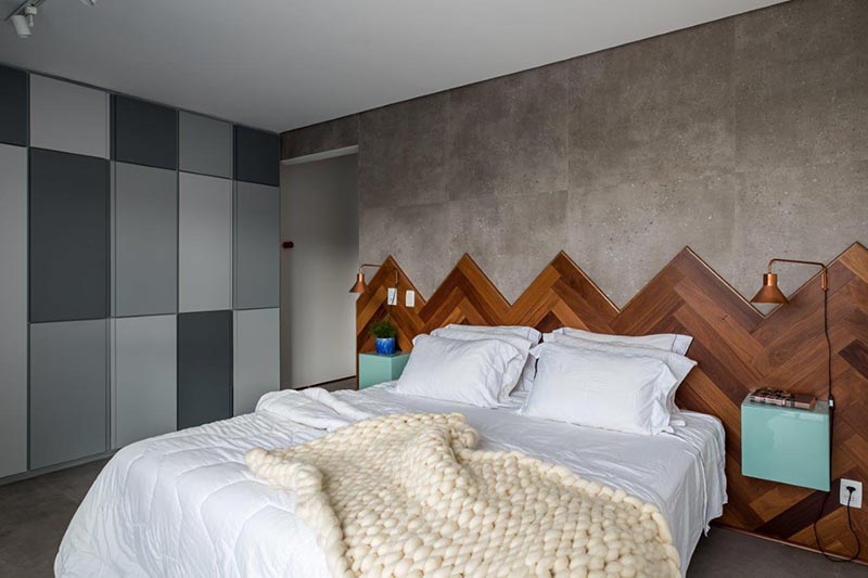 This modern wood headboard, with its different shades of wood laid in a herringbone pattern, travels the entire length wall, adding visual interest to the room, and softening the concrete wall and floor of the bedroom. #WoodHeadboard #Herringbone #ModernBedroom #HeadboardIdeas