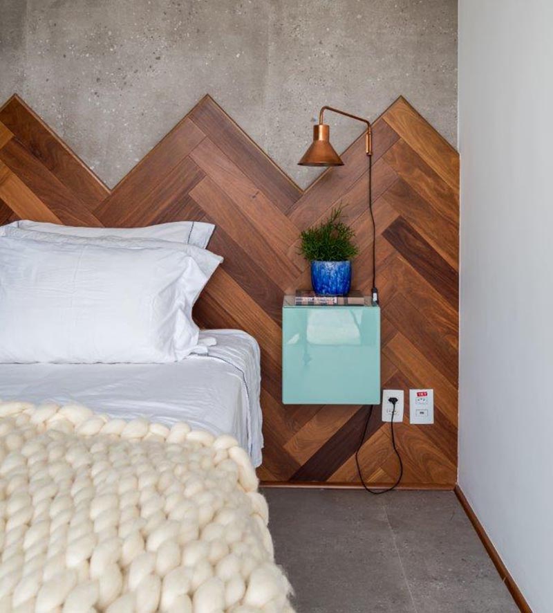 This modern wood headboard, with its different shades of wood laid in a herringbone pattern, travels the entire length wall, adding visual interest to the room, and softening the concrete wall and floor of the bedroom. #WoodHeadboard #Herringbone #ModernBedroom #HeadboardIdeas