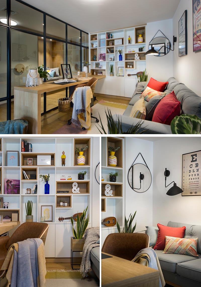 Inside this modern glass-enclosed home office is a long wood desk that meets a custom-designed bookshelf, with some of the shelves lined with wood. Opposite the desk is a comfortable grey couch, a few plants, and colorful pillows, while a rug adds a soft touch underfoot. #HomeOffice #GlassWalls #Shelving