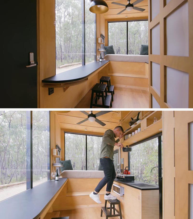 In the kitchen of this modern tiny house, there's everything you need from a gas stove to a small fridge. Opposite the kitchen is a breakfast bar, whose stools double as stairs to reach the open shelving in the kitchen. #TinyHouse #TinyHome #BreakfastBar #SmallKitchen