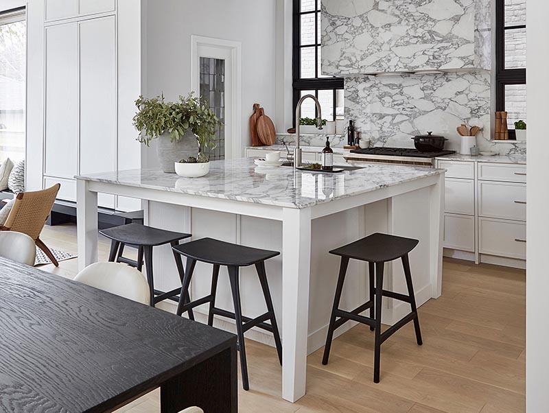 By having a square kitchen island with a white and marble finish, the designers of this kitchen were able to include four spaces for seating in the form of counter stools, which is ideal if you're entertaining and want to interact with the person cooking, or if you need a spot to have a quick bite to eat. #SquareIsland #SquareKitchenIsland #KitchenDesign #KitchenIsland #IslandWithSeating