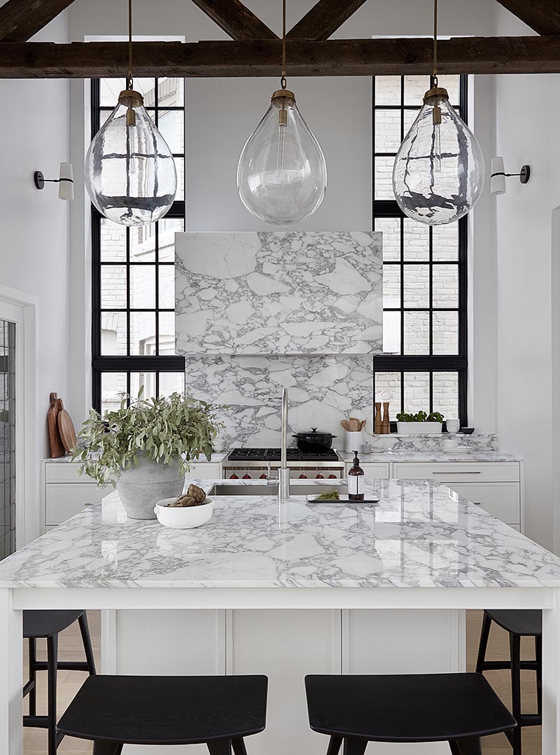 By having a square kitchen island with a white and marble finish, the designers of this kitchen were able to include four spaces for seating in the form of counter stools, which is ideal if you're entertaining and want to interact with the person cooking, or if you need a spot to have a quick bite to eat. #SquareIsland #SquareKitchenIsland #KitchenDesign #KitchenIsland #IslandWithSeating