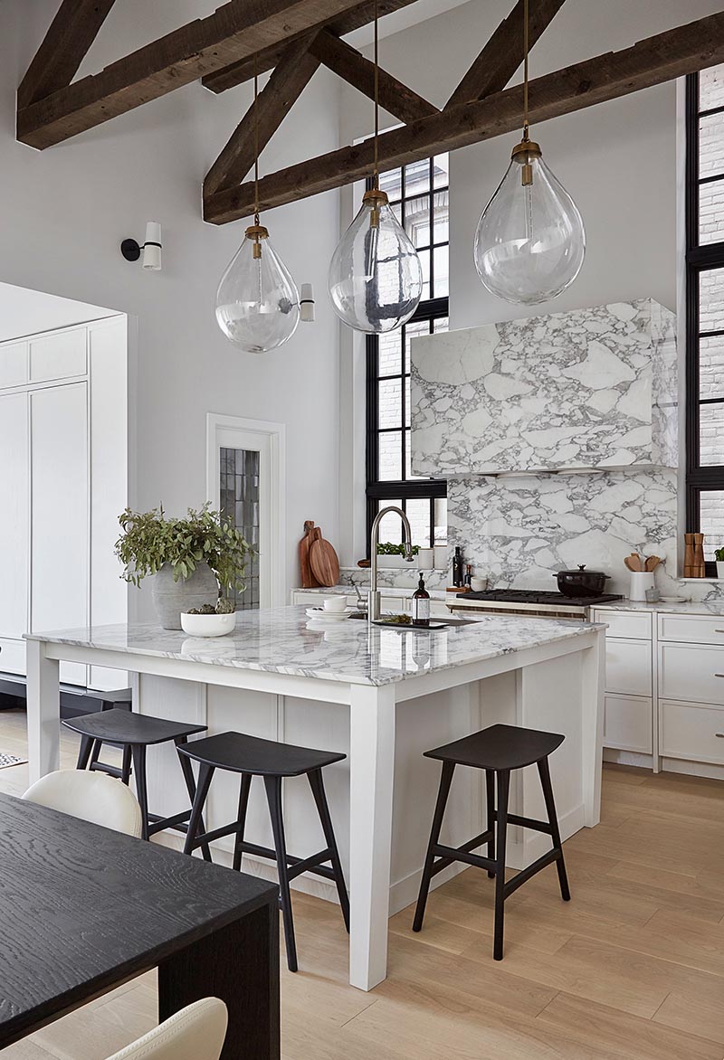 By having a square kitchen island with a white and marble finish, the designers of this kitchen were able to include four spaces for seating in the form of counter stools, which is ideal if you're entertaining and want to interact with the person cooking, or if you need a spot to have a quick bite to eat. #SquareIsland #SquareKitchenIsland #KitchenDesign #KitchenIsland #IslandWithSeating